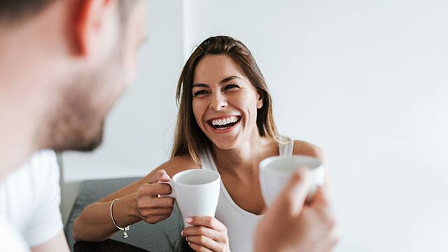 A happy couple holding white cups indoors