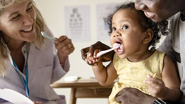 parent brushing his babies teeth in front of dentist